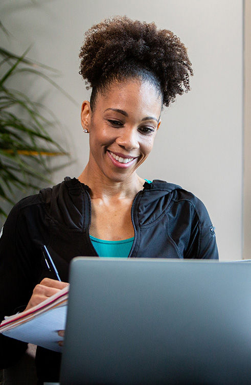 Aspiring ACE Specialist studying online with laptop and notebook, excited to grow her health and fitness career