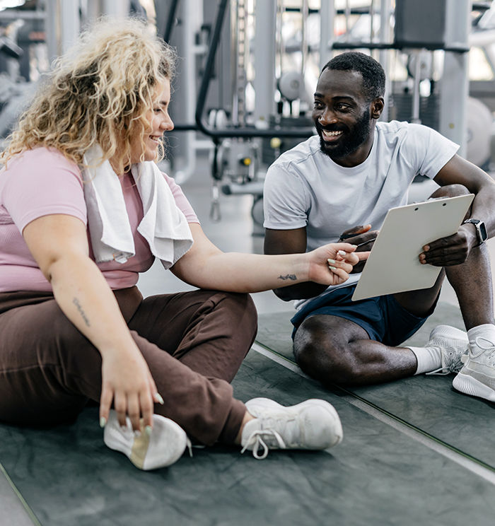 ACE Weight Management Specialist coaching an overweight client in a gym, reviewing progress data on a clipboard