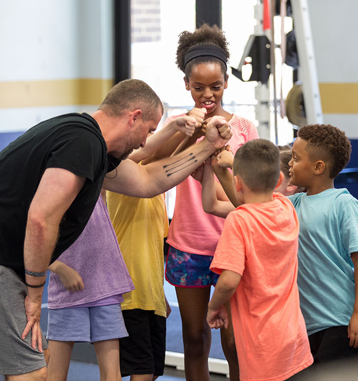 ACE Youth Fitness Specialist leading a group of kids in a fitness setting, all reaching in for a group fist bump
